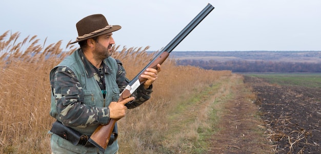 Un chasseur avec une arme à feu dans ses mains dans des vêtements de chasse dans la forêt d'automne à la recherche d'un trophée Un homme se tient avec une arme