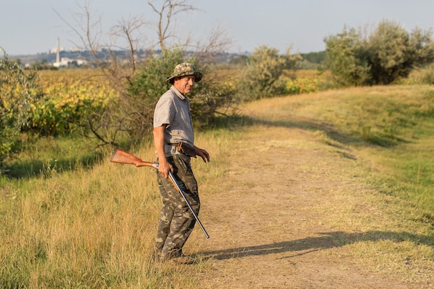 Un chasseur avec une arme à feu dans ses mains dans des vêtements de chasse dans la forêt d'automne à la recherche d'un trophée