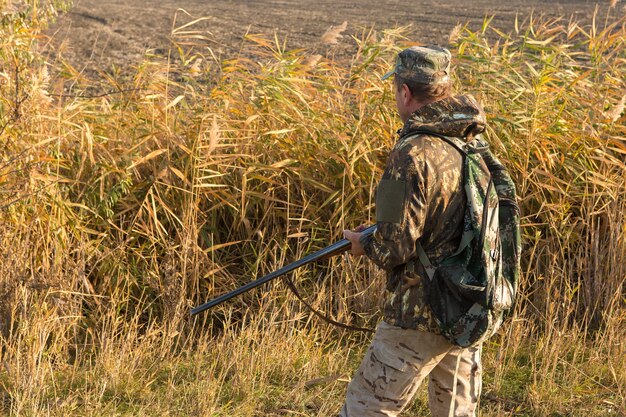 Un chasseur avec une arme à feu dans ses mains dans des vêtements de chasse dans la forêt d'automne à la recherche d'un trophée