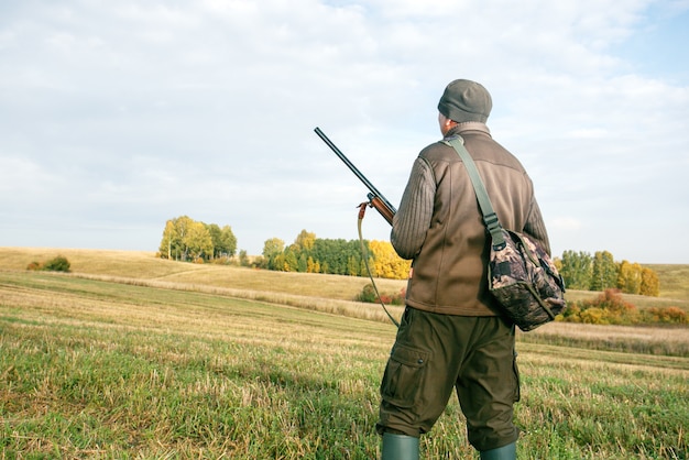 Un chasseur avec une arme à feu dans ses mains pour chasser dans une forêt et un champ d'automne