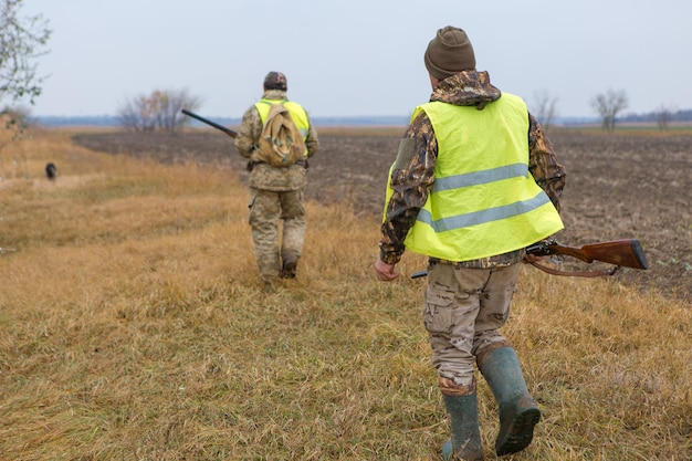 Un chasseur avec une arme à feu dans ses mains en vêtements de chasse dans la forêt d'automne à la recherche d'un trophée Un homme se tient avec des armes et des chiens de chasse traquant le gibier