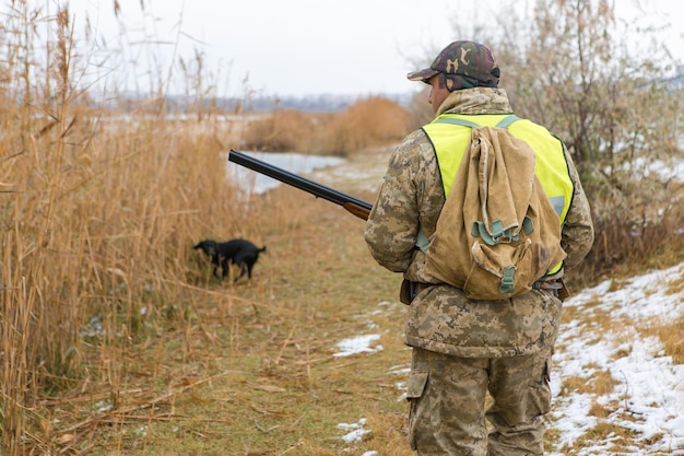 Un chasseur avec une arme à feu dans ses mains en vêtements de chasse dans la forêt d'automne à la recherche d'un trophée Un homme se tient avec des armes et des chiens de chasse traquant le gibier