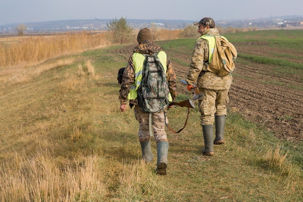 Un chasseur avec une arme à feu dans ses mains en vêtements de chasse dans la forêt d'automne à la recherche d'un trophée Un homme se tient avec des armes et des chiens de chasse traquant le gibier