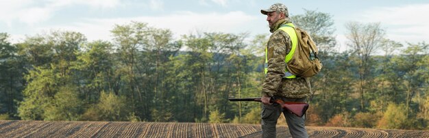 Un chasseur avec une arme à feu dans ses mains en vêtements de chasse dans la forêt d'automne à la recherche d'un trophée Un homme se tient avec des armes et des chiens de chasse traquant le gibier