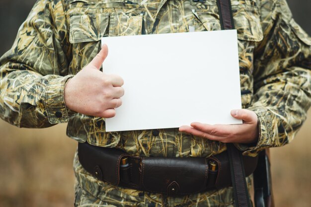 Un chasseur avec une arme à feu, il garde un formulaire blanc pour la publicité sur fond de forêt d'automne