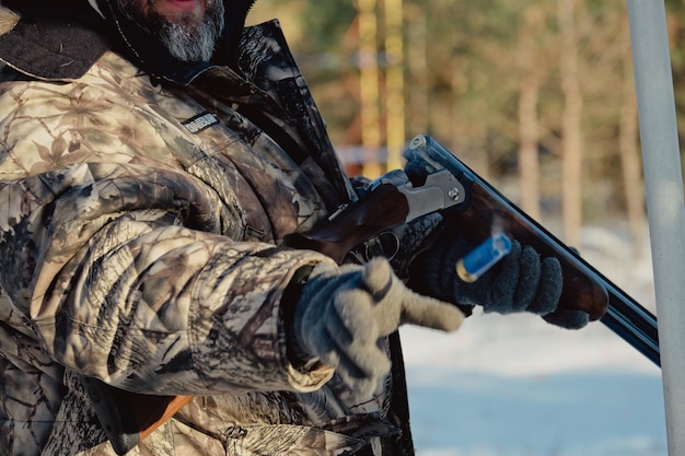 Chasseur en camouflage avec fusil dans la forêt d'hiver. Concept de chasse. Homme sécurisant une réserve, un jour de neige. Hunter vise d'une arme à feu dans la forêt enneigée