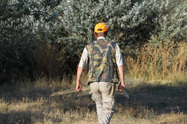 Chasseur de canard avec fusil de chasse marchant dans un pré xARvue arrière d'un homme avec une arme dans les mains