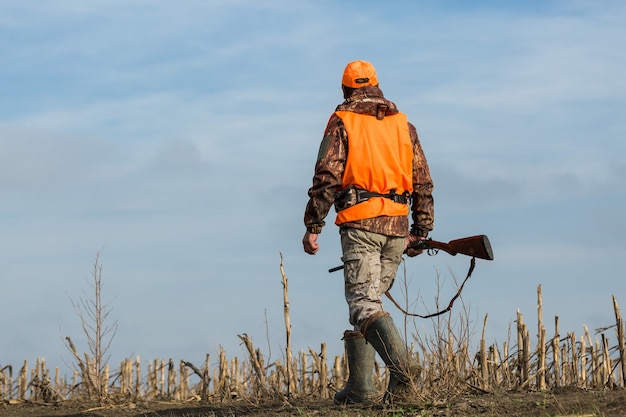 Chasseur de canard avec fusil de chasse marchant dans un pré.