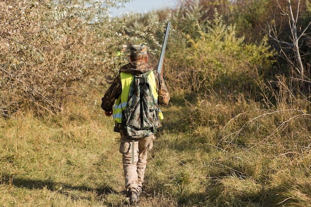 Chasseur de canard avec fusil de chasse marchant dans un pré