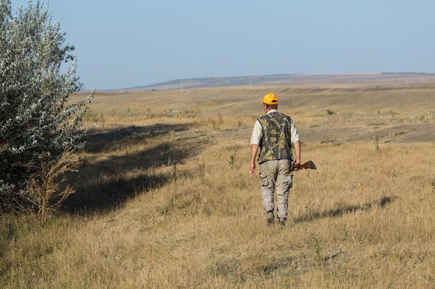 Chasseur de canard avec fusil de chasse marchant dans un pré