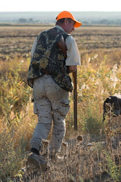 Chasseur de canard avec fusil de chasse marchant dans un pré.