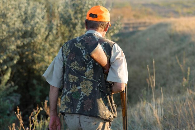 Chasseur de canard avec fusil de chasse marchant dans un pré.