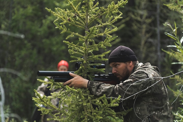 Le chasseur est assis dans une embuscade avec une carabine dans les mains. Le gars se prépare à tirer avec un fusil de sniper