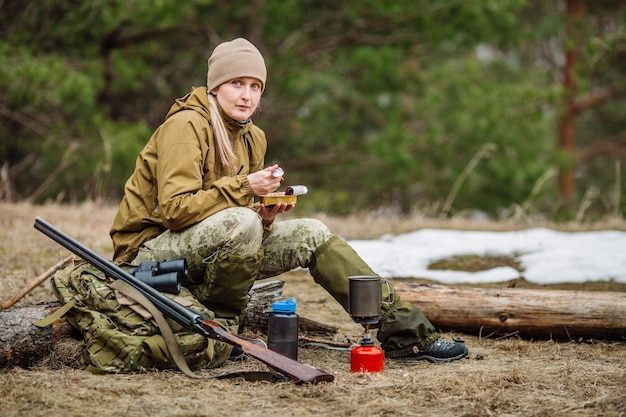 Chasseur féminin préparant la nourriture avec un brûleur à gaz portatif dans une forêt d'hiver