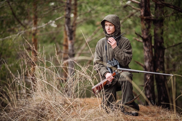 Chasseur mâle avec des jumelles prêt à chasser tenant un pistolet et marchant dans la forêt