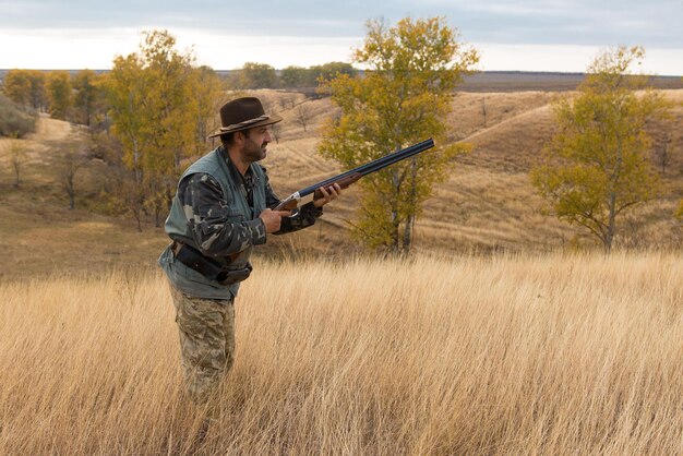 Chasseur en tenue de camouflage avec une arme à feu pendant la chasse à la recherche d'oiseaux sauvages ou de gibier Saison de chasse d'automne