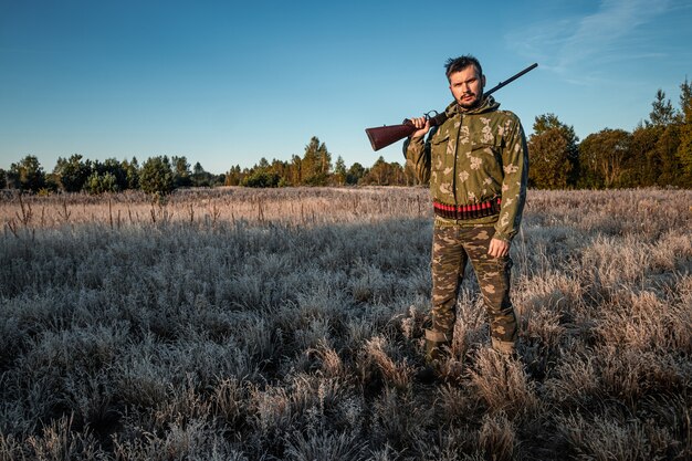 Chasseur en tenue de camouflage avec une arme à feu pendant la chasse à la recherche d'oiseaux sauvages