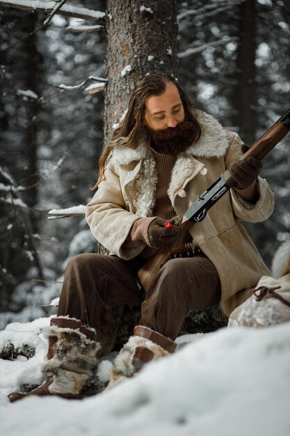 Chasseur en vêtements vintage d'hiver avec barbe en forêt avec pistolet