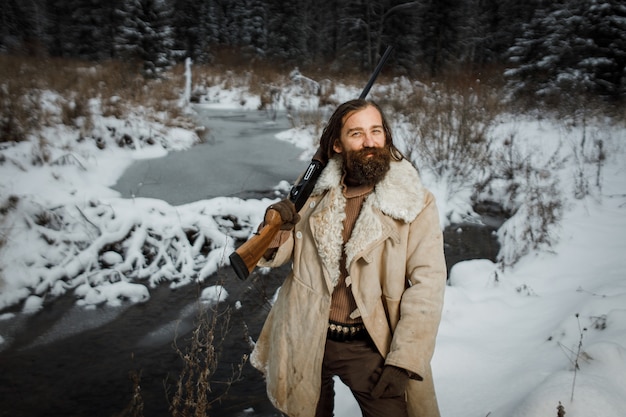 Chasseur en vêtements vintage d'hiver avec barbe en forêt avec pistolet