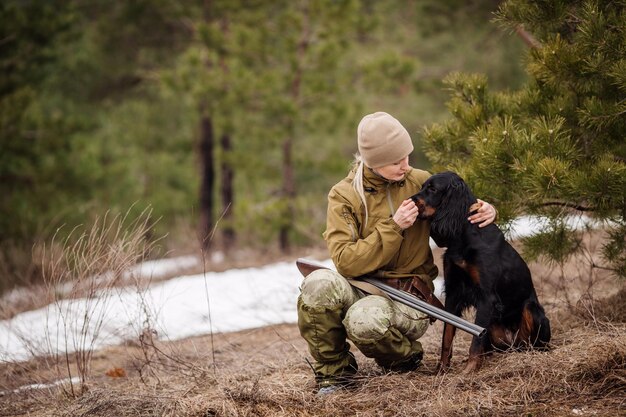 Chasseuse en tenue de camouflage prête à chasser tenant une arme à feu et marchant dans la forêt