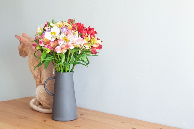 Chat de Cornouailles beige avec un bouquet de fleurs dans un vase sur une table en bois