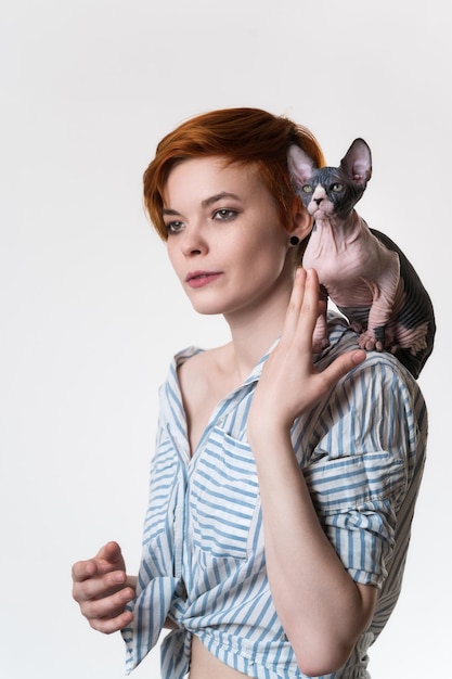 Chat sans poils Sphynx assis sur l'épaule d'une jeune femme rousse hipster femelle aux cheveux courts dresse