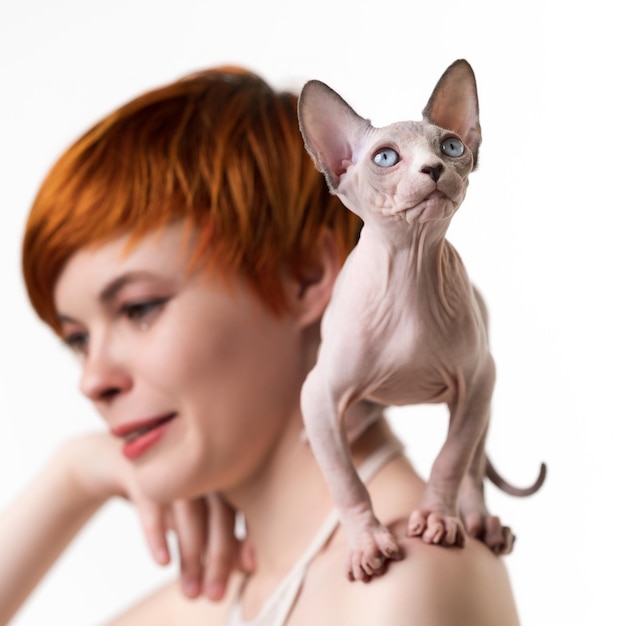 Chat Sphynx espiègle regardant vers le haut se dresse sur l'épaule jeune femme rousse mise au point sélective sur le premier plan