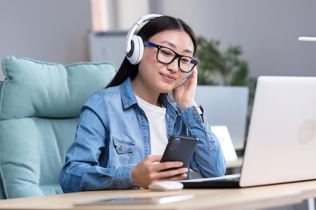 Chat vidéo avec des amis jeune belle femme asiatique portant des écouteurs tenant un téléphone dans sa main