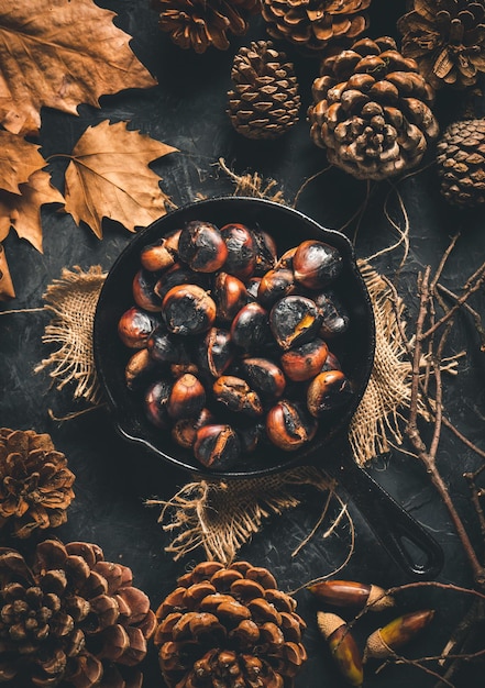 Châtaignes grillées dans une petite poêle en fer sur une table avec des feuilles d'automne et des pommes de pin