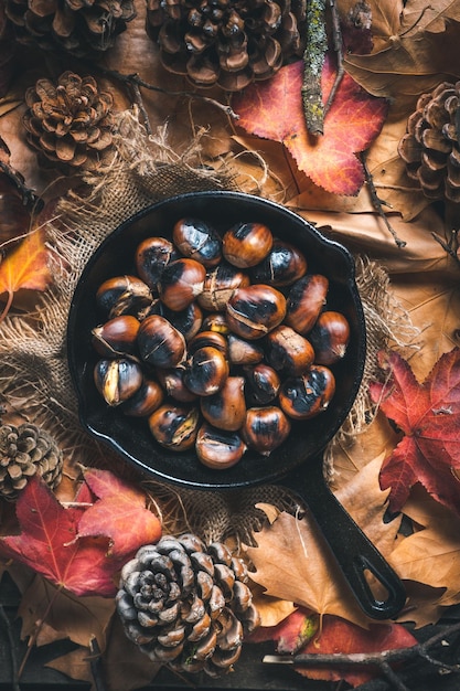 Châtaignes grillées dans une petite poêle en fer sur une table avec des feuilles d'automne et des pommes de pin