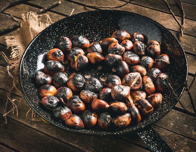 Châtaignes grillées dans une poêle à châtaignes avec des trous sur une table en bois brun vieilli