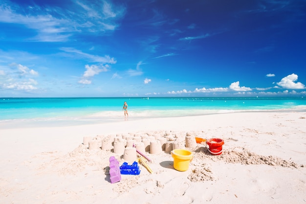 Château de sable à la plage de sable blanc avec des jouets pour enfants en plastique et la mer