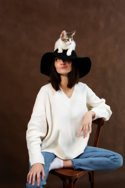 Le chaton blanc s'assied sur le chapeau avec une grande tête de bord d'une jeune femme