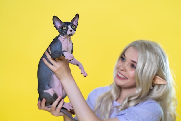 Chaton de race sphynx est entre les mains d'une jeune femme elfe cosplay qui sourit démontrant l'ani préféré