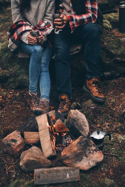 Chaud et confortable. Gros plan d'un jeune couple tenant des tasses en se réchauffant près du feu de camp