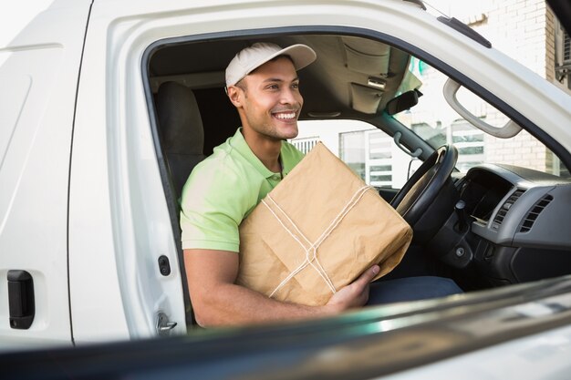 Chauffeur de livraison souriant dans sa camionnette tenant le colis