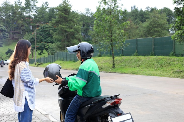 Photo un chauffeur de moto-taxi ojek en ligne donne un casque à une cliente