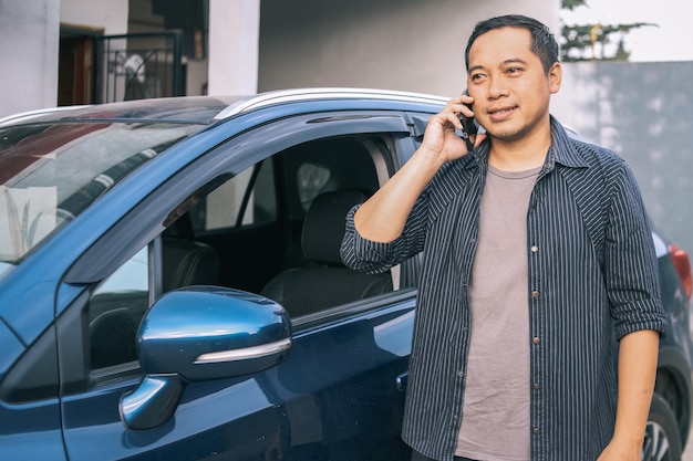 Chauffeur de taxi asiatique, homme debout devant sa voiture, ayant un appel téléphonique avec ses clients