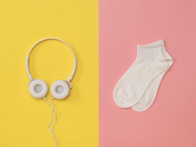 Chaussettes blanches et écouteurs blancs sur fond jaune et rose. La tendance couleur. Le concept de la musique et du sport. Mise à plat.