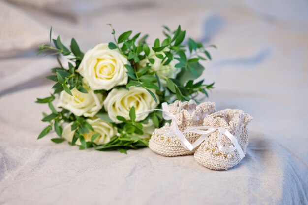 Chaussons bébé et fleurs sur un plaid en lin ajouré. En attendant bébé-fille. Grossesse, maternité.