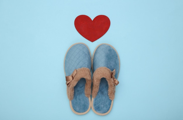 Chaussons de couchage confortables pour femmes et coeur sur fond bleu pastel. Vue de dessus