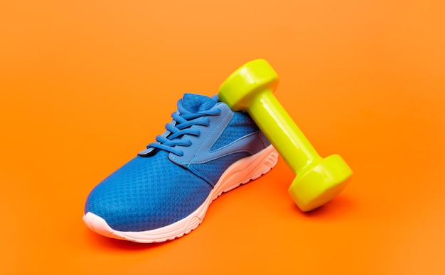 Chaussure de sport bleue confortable avec haltères sur fond orange, accessoire de sport.