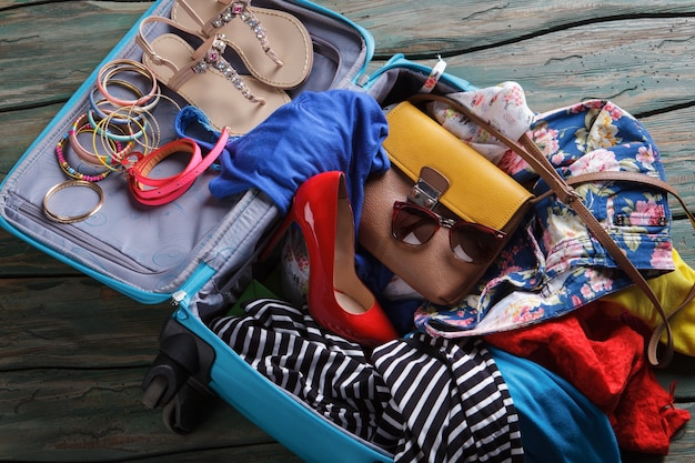 Chaussure à talon rouge dans une valise. Vêtements froissés dans un sac à bagages. Il n'y a jamais assez de place. Pensez à acheter une valise plus grande.