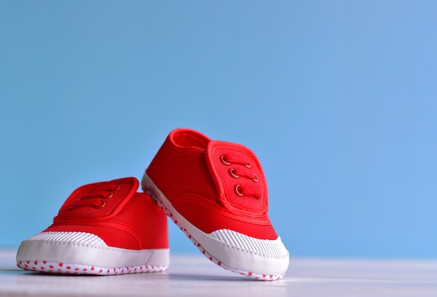 Chaussures bébé rouge sur un plancher en bois blanc et fond bleu