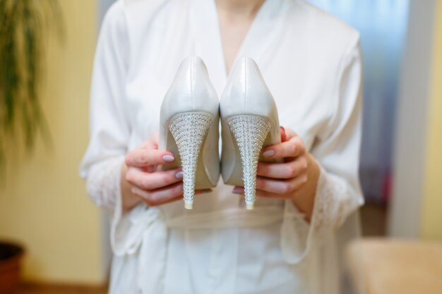 Chaussures blanches à talons dans les mains de la mariée