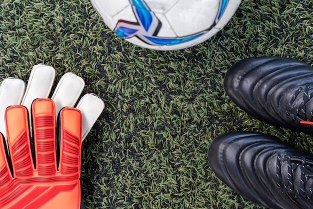 Chaussures à crampons de football avec ballon de foot et gant sur terrain en gazon synthétique