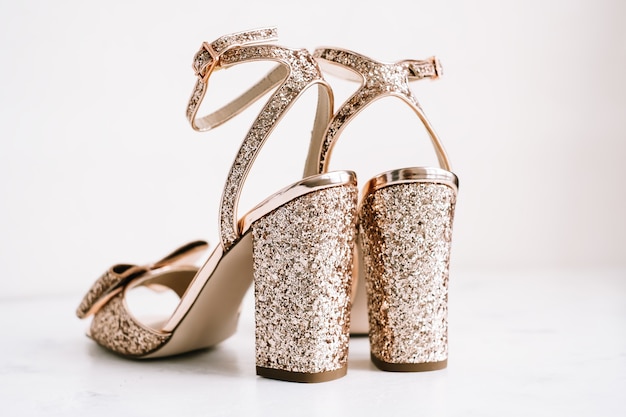 Chaussures femmes dorées à talons et paillettes sur fond blanc.