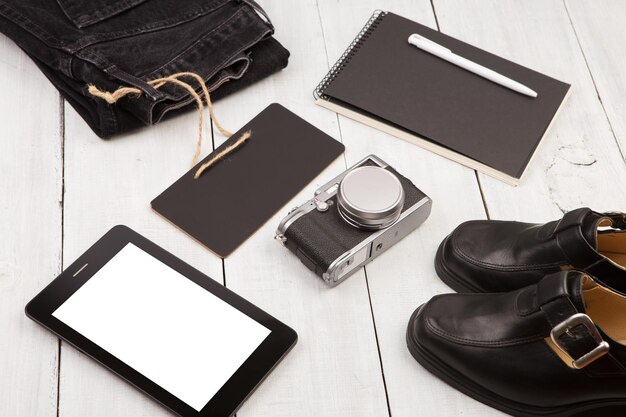 Chaussures jeans tablet pc caméra bloc-notes et tableau noir sur un bureau en bois blanc