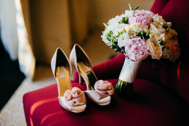 Chaussures de mariée et bouquet de mariée avec des fleurs douces sur une chaise rouge