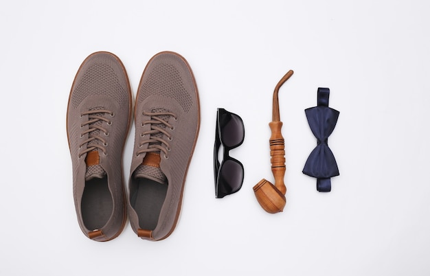 Chaussures pour hommes, pipe, lunettes de soleil et noeud papillon sur fond blanc. Accessoires de gentleman. Vue de dessus